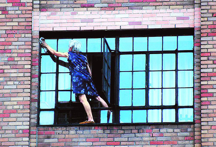 Пожилая женщина моет окно снаружи