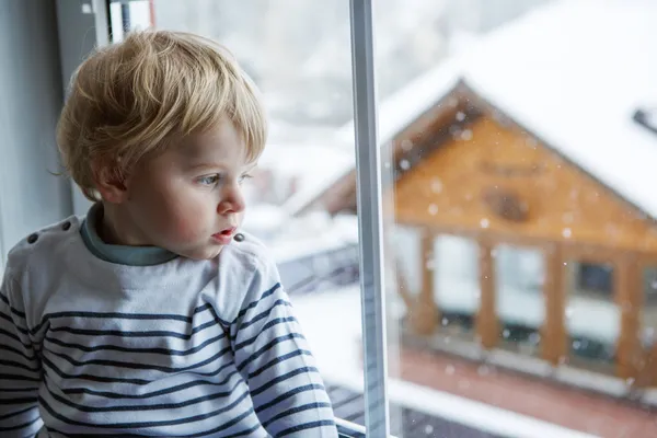 Малыш мальчик смотрит в окно в зимний день с — стоковое фото