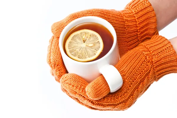 Руки в оранжевый вязаные варежки, держа чашку чая с лимоном — стоковое фото