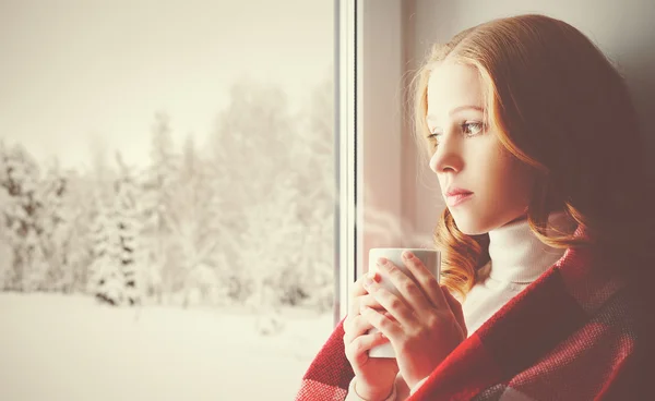Задумчивый Грустная девушка с бокалом потепления, глядя в окно, в — стоковое фото