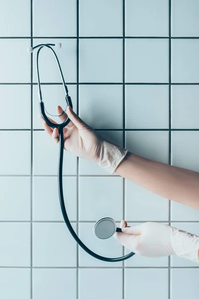 Cropped Shot Doctor Gloves Holding Stethoscope Front Tiled White Wall — стоковое фото