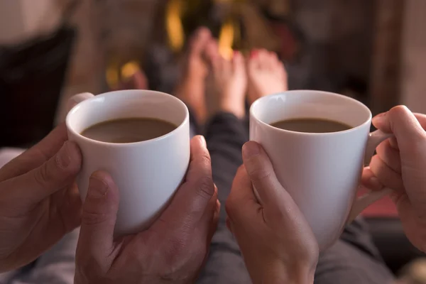 Ноги, нагревающиеся в камине руками, держащими кофе — стоковое фото
